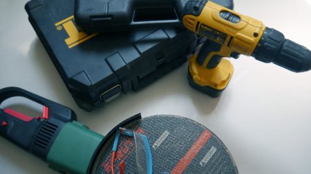 A green angle grinder sits next to a yellow power drill and a pair of goggles.