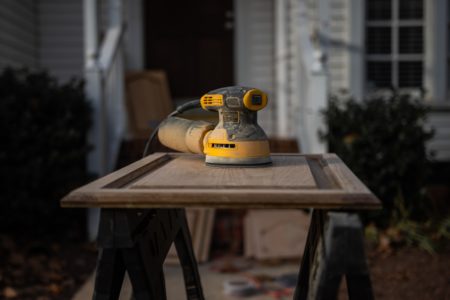 A yellow and black orbital sander ready to work on a cupboard door
