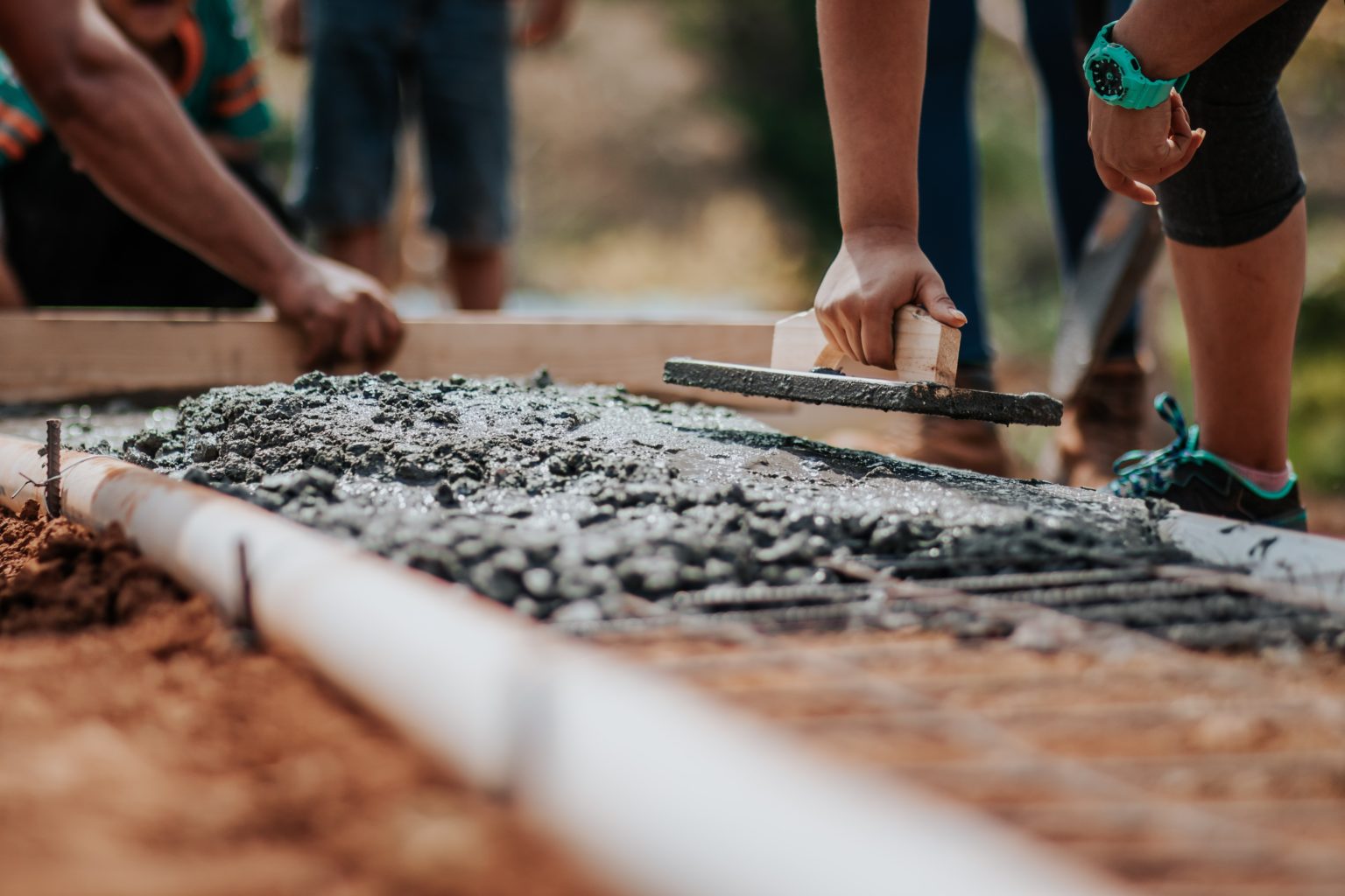 People smoothing wet concrete inside of a wooden mold.