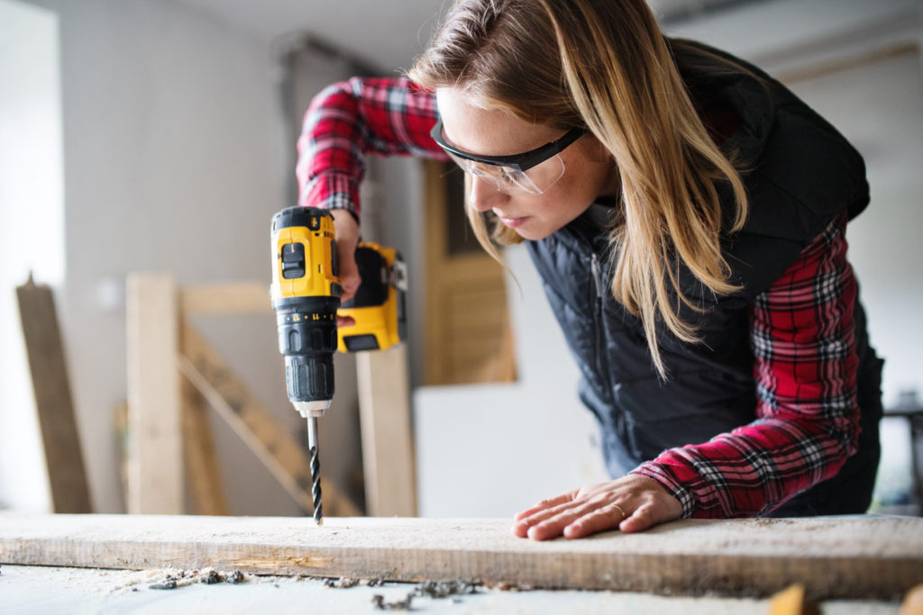 Young woman worker in workroom. Female carpenter using drill.