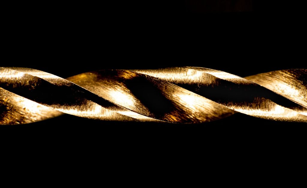 A close-up of a brass-colored spiral drill bit against a black background