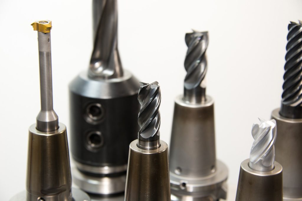 Several different types of drill bits, each sticking vertically out of a drill, on a white background