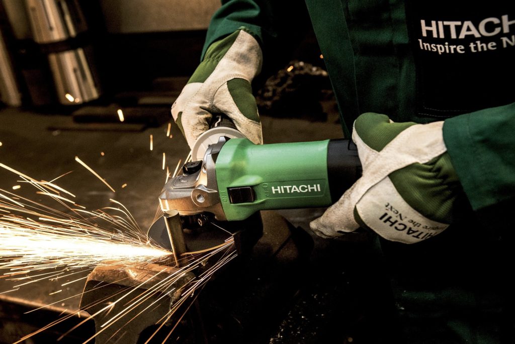 A worker wearing protective gloves uses a power grinder to cut metal.