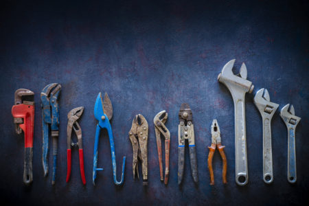 Aged construction hand tools inventory pliers nippers, wrenches, grip, pipe wrench organized in a row on dark gray grunge background.