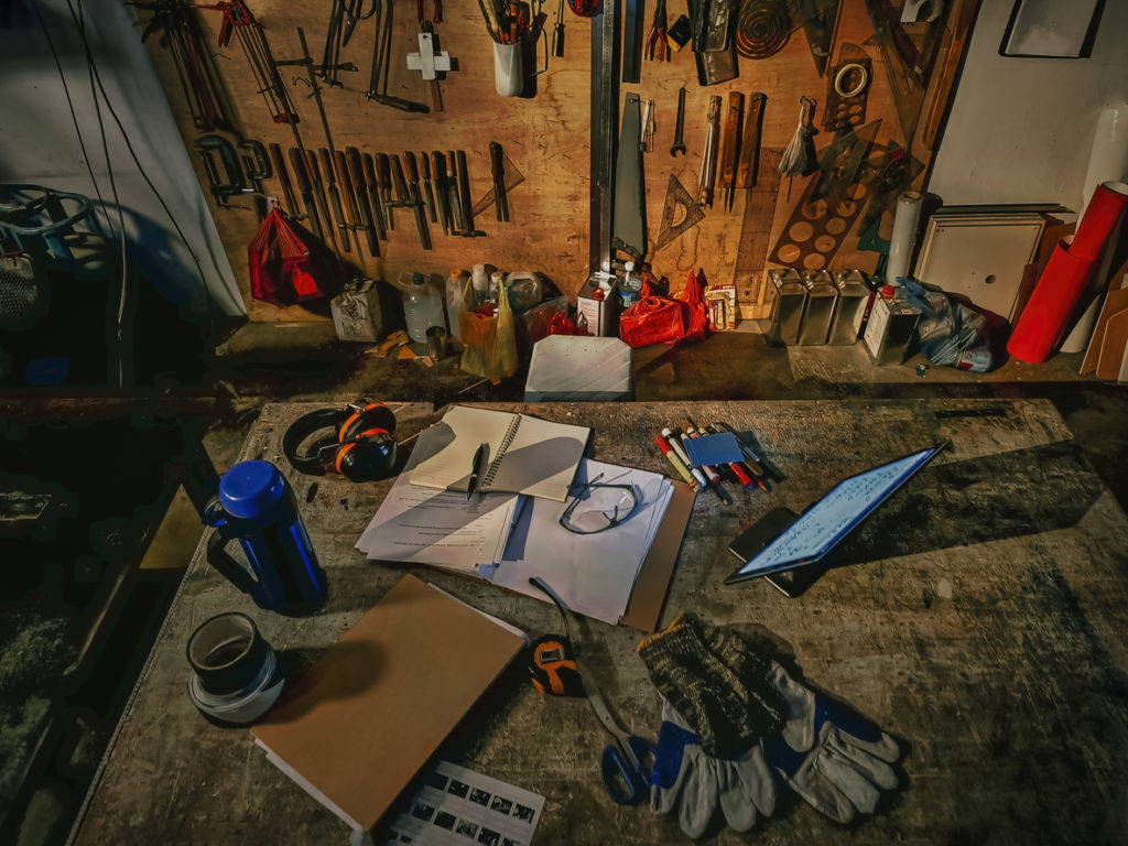 directly above workshop workbench table with documents , digital table, pens, safety equipment and travel mug.