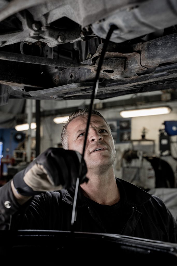 A man wearing black clothes and gloves drains the oil from an engine into a drip pan.